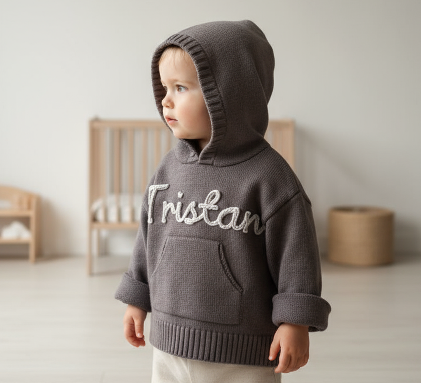 Child wearing a gray hoodie with 'Tristan' embroidered on it, standing in a minimalistic room.