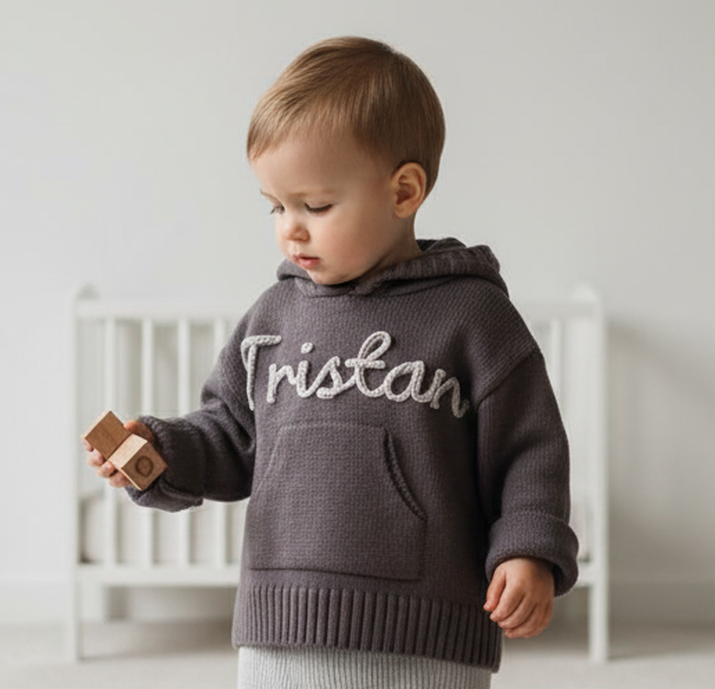 Child wearing a dark gray hoodie with 'Tristan' printed on it, holding wooden blocks.
