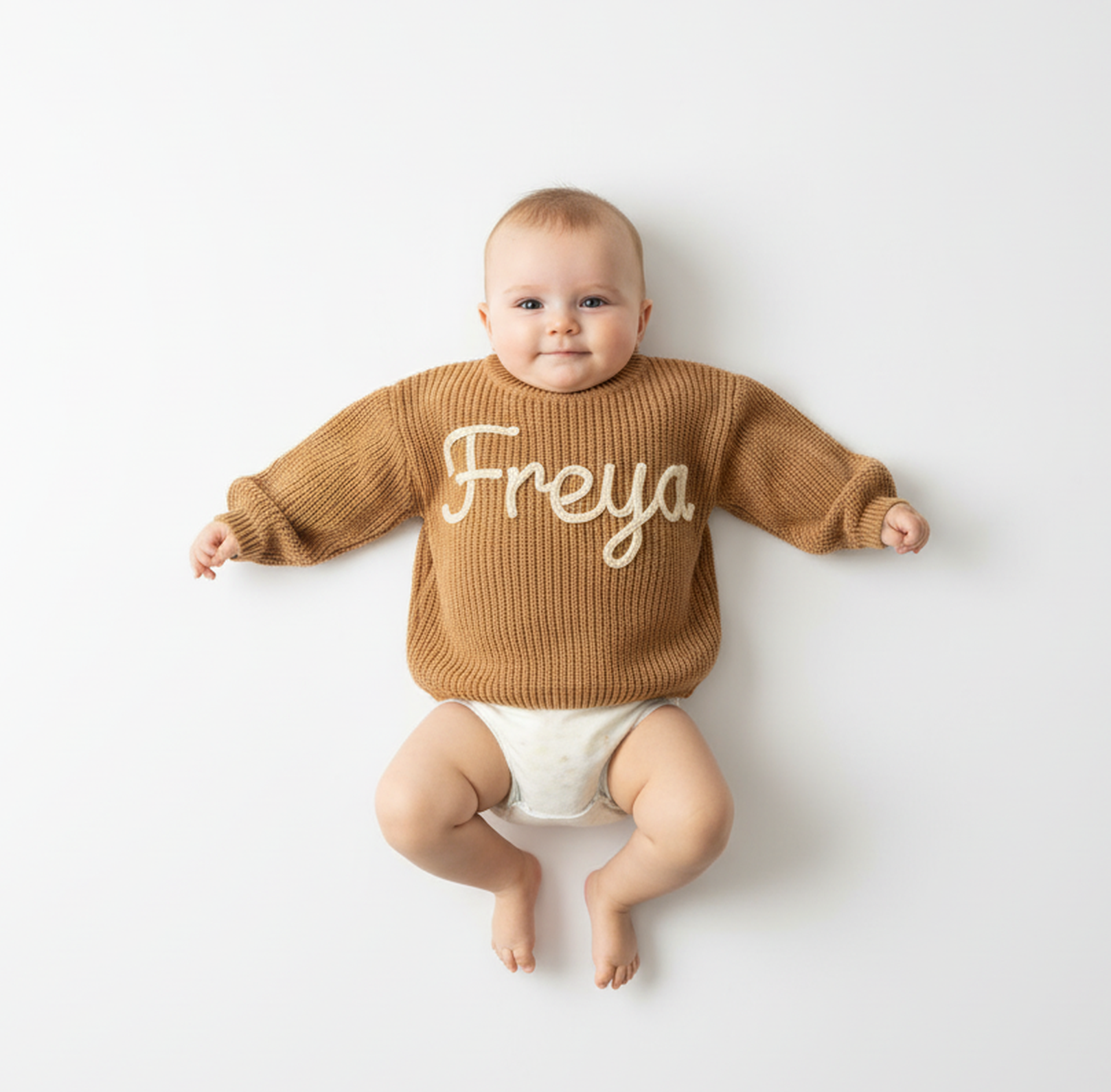 Baby wearing a brown sweater with 'Freya' printed on it, sitting on a white background