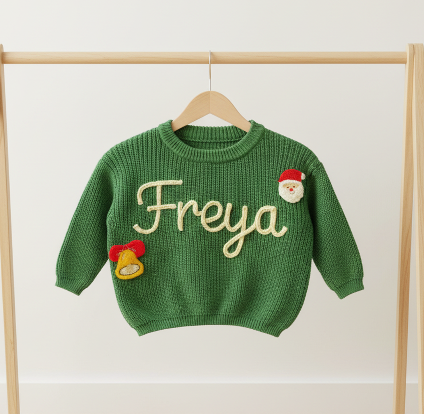 Green sweater with 'Freya' embroidered on it, hanging on a wooden rack.