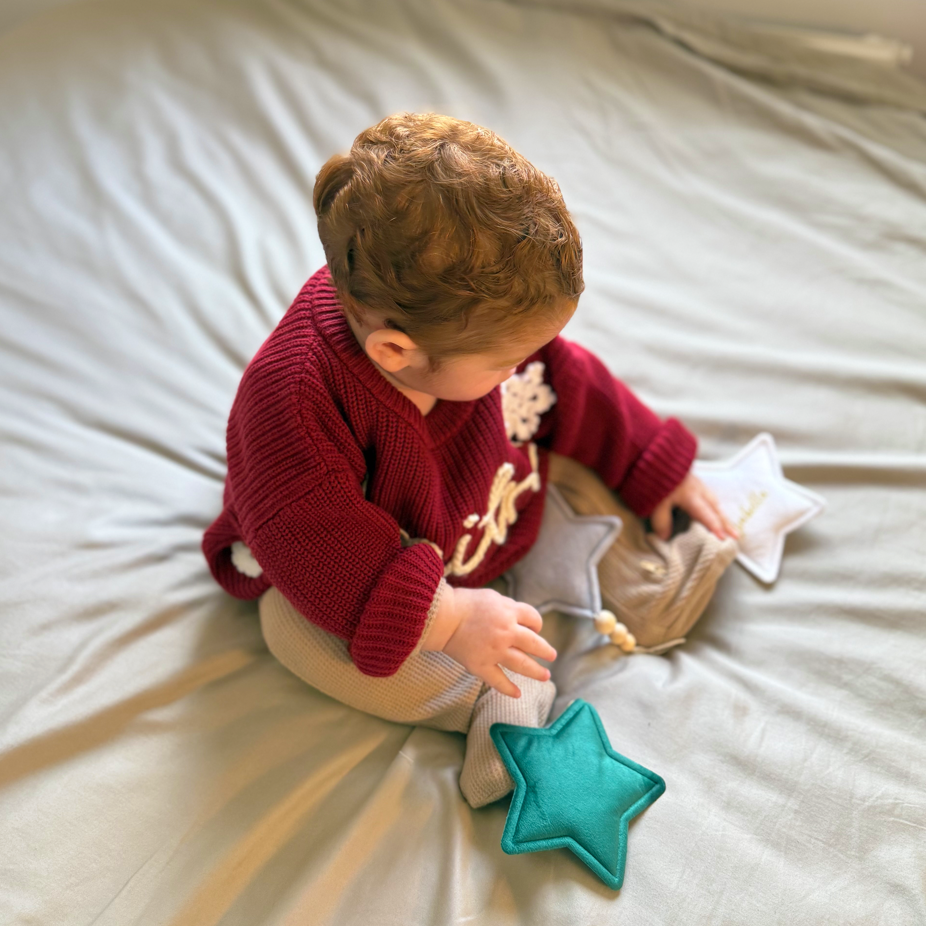 Child in a red sweater playing with star-shaped toys on a light-colored surface